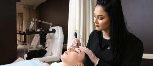 One female Esthetician student applies a skin treatment to another student in the о salon spa.